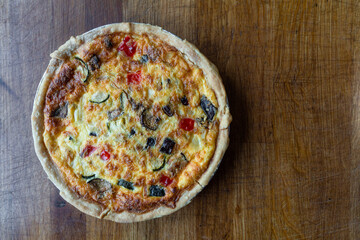Quiche. Fresh eggs mixed with vegetables, bacon, ham, sausage, cheese, and Broccoli. The round shape on rustic wooden board.