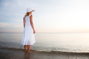 Fototapeta na wymiar Woman in hat and white dress on the beach