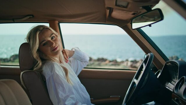 Cute blonde sitting automobile holding smartphone close up. Girl looking camera.