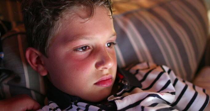 Boy face at night in front of tablet screen, blue light glowing into child eyes while watching content