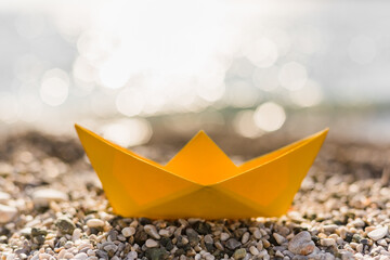 Yellow paper boat on the pebble beach