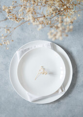 Obraz na płótnie Canvas Table setting in a minimalist style with white plate and a bouquet of gypsophila on a blue background. Top view