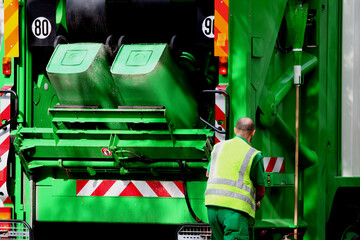 Green garbage truck and cleaning worker in the street