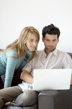 Young professional man working at home with his laptop on the sofa and his partner looking on.