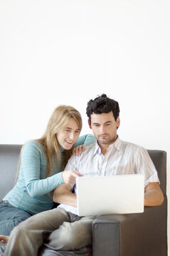A young couple at home on the sofa excited about what they're seeing on their laptop computer