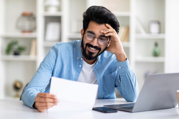 Naklejka premium Young Indian Male Self-Entrepreneur Working With Papers At Desk In Home Office