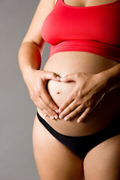 Pregnant women wrap her arms around the belly in the form of the heart. Isolated on white.