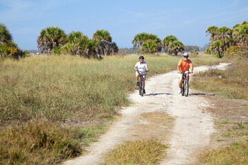 Obraz premium Senior couple riding their bikes on a trail beside the beach.