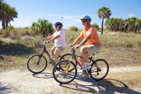 Senior couple riding bikes at the beach, wearing sunglasses and helmets.  Focus on the woman.