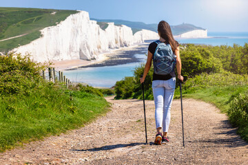 A female hiker walks down a path towards the famous Seven Sisters chalk cliffs in Sussex, England