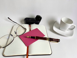 Clean environment with fountain pen, notepad, agenda, glasses, cup and saucer