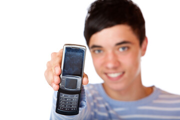 Young handsome teeanger smiles happy and holds mobile phone into camera. Isolated on white.