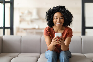 Young Smiling Black Woman With Smartphone Resting On Couch At Home