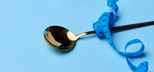 Empty spoon wrapped with centimeter on blue background, weight loss concept