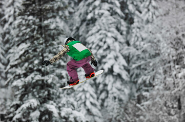 young boys jumping in air ind showing trick with snowboard at winter season