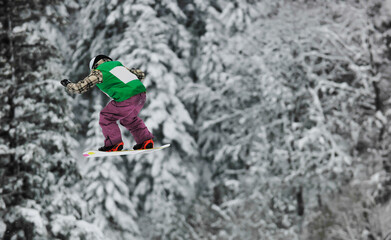 young boys jumping in air ind showing trick with snowboard at winter season