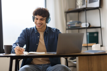 Middle Eastern Man At Laptop Taking Notes Wearing Earphones Indoor