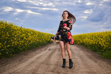 Fototapeta premium Beautiful latino woman in floral dress in a canola field