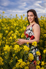 Beautiful latino woman in floral dress in a canola field