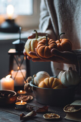 Autumn home composition with aromatic candles. Woman in wool sweater holding a pumpkin....