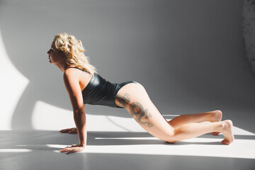 Plakat a sexy blonde with tattoos in a leather swimsuit performs sports exercises 
