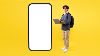 Student Using Laptop Posing With Huge Phone On Yellow Background