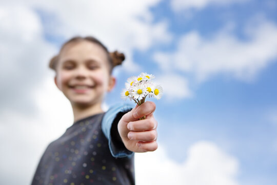 Little girl with bouquet of daisies in front of sky background. 