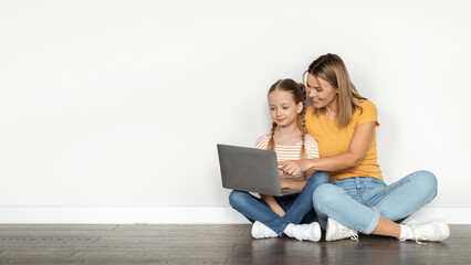 Smiling mother and cute little daughter using laptop together at home - Powered by Adobe
