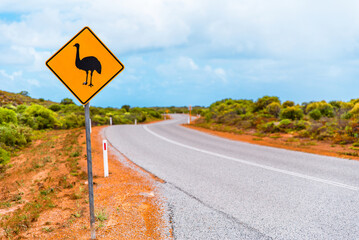 Beware of emu road sign in Australian outback. Yellow warning sign on winding asphalt road in Australia