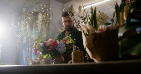 Professional florist entrepreneur adds beautiful and fresh flowers to bunch. Man creates multi color bouquet with plants to sale in flower shop. Concept of retail floral business and entrepreneurship.