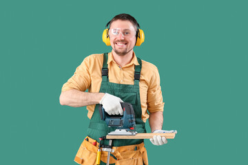 Male carpenter sawing wooden plank with jigsaw on green background - obrazy, fototapety, plakaty