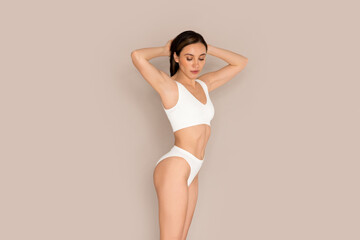 Obraz premium Slim attractive young woman demonstrating perfect body on beige