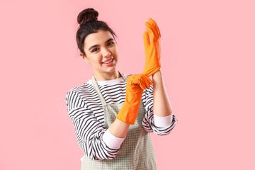 Young woman putting on rubber gloves on pink background