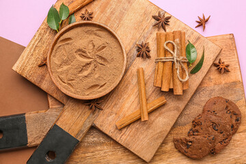 Wooden boards with bowl of cinnamon powder, sticks, anise stars and cookies on color background, closeup
