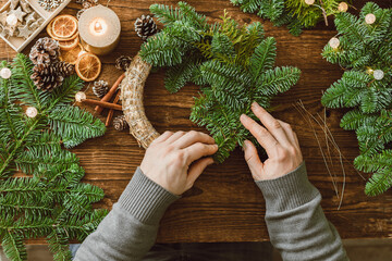 Top view of the hands of a male florist making a Christmas wreath from natural materials. Decorations for Christmas and New Year