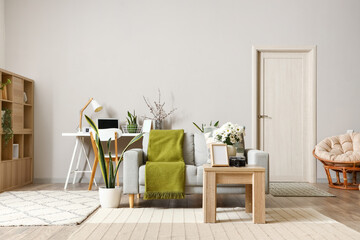 Interior of modern living room with grey sofa, workplace and blooming chrysanthemum flowers on table