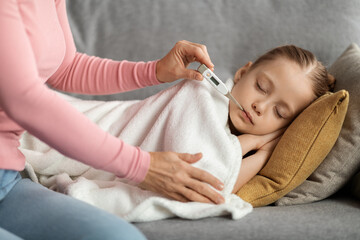 Mother Measuring Temperature Of Her Ill Daughter With Oral Thermomether At Home