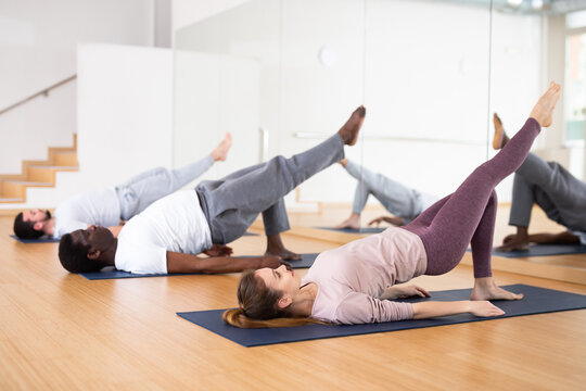 Men and woman lying on mats in gym and doing leg exercises.