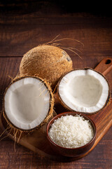 Whole coconut, pieces of coconut and shredded coconut on the table.