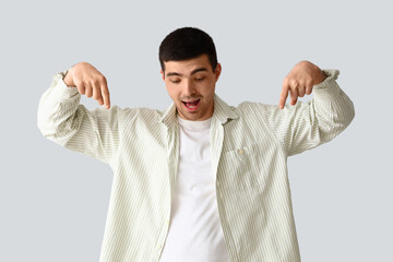 Young man pointing at something on light background