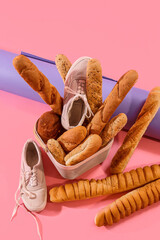 Sportive male sneakers with basket of bread on pink background