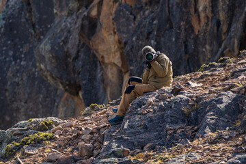 Nature photographer sitting on a rock taking a picture. Front view