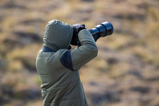 Nature photographer with green jacket using a telephoto lens. Rear view