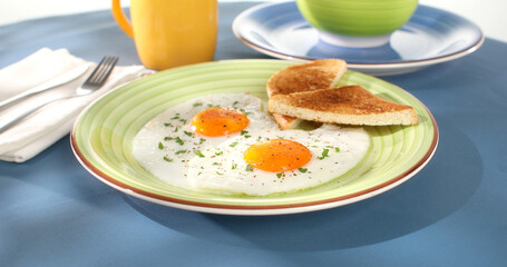 fried eggs with toast on a green plate. close-up. angle view. camera tracking. blue background. traditional breakfast. sunny day.