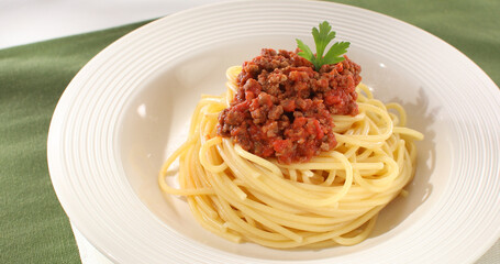 spaghetti bolognese on a white plate. classic italian pasta with meat tomato sauce on a green background. dish of mediterranean cuisine. food on the table on a sunny day. yellow noodles, minced meat.