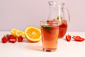 Glass and jug of tasty strawberry juice on white table