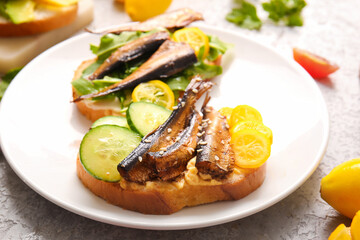 Plate of tasty sandwiches with canned smoked sprats on table