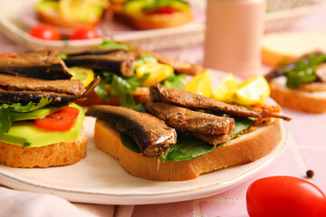 Plate of tasty sandwiches with canned smoked sprats on table, closeup
