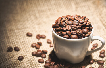 Cup full of coffee beans on sisal fabric