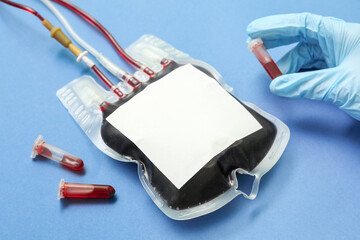 Female doctor with tube and blood pack on blue background, closeup. World Donor Day